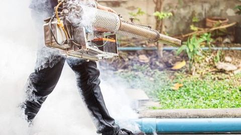 Técnico con máquina de nebulización generando humo insecticida junto a una zona ajardinada en Control de Plagas León