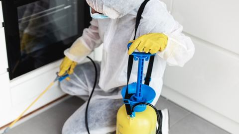 Técnico con equipo de protección aplicando insecticida junto al horno de una cocina en Control de Plagas León