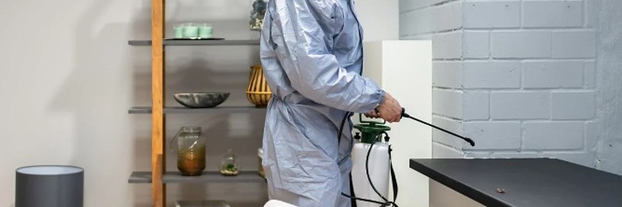 Técnico con equipo de protección aplicando tratamiento junto a una encimera de cocina en un servicio de control de plagas en Valencia de Don Juan